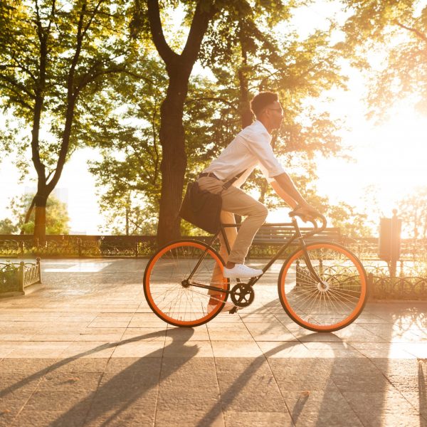 Image of young african man early morning with bicycle walking outdoors. Looking aside.
